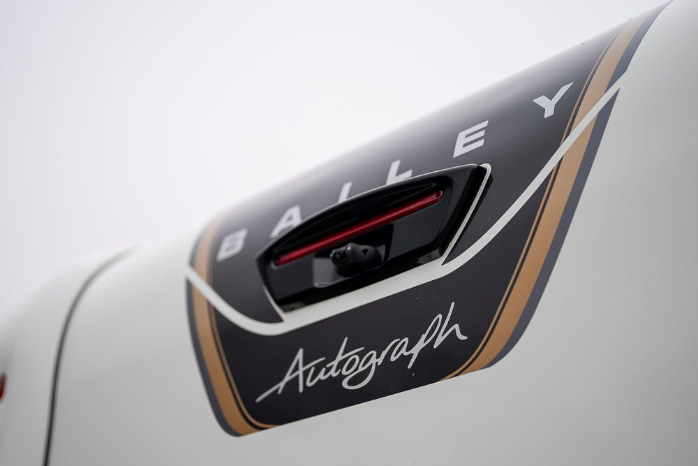 Close-up of the rear of a white 2022 Bailey Autograph 74-4, displaying the brand "Bailey" and model name "Autograph" with a decorative black and gold design. A small rear camera is positioned above the model name.