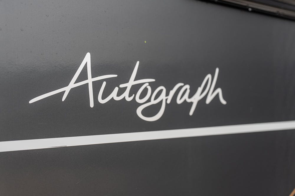 Close-up of the word "Autograph" written in a white cursive font on a dark grey surface with a white horizontal line below it, reminiscent of the elegance found in the 2022 Bailey Autograph 74-4.