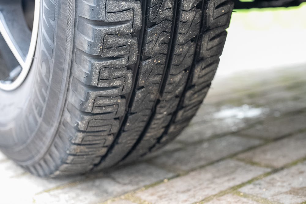Close-up image of a car tire with a detailed view of the tread pattern, part of the robust 2022 Bailey Autograph 74-4. The tire is resting on a brick-paved surface, with small particles of dirt visible on the tread. The surrounding area is slightly blurred.