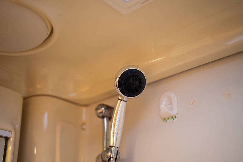 A close-up view of a showerhead mounted on the wall of a bathroom in the 2007 Auto-Sleepers Sigma EL. The metallic showerhead has a black spray face and is attached to an adjustable arm. The surrounding wall is beige, with a soap dish and part of the ceiling visible.