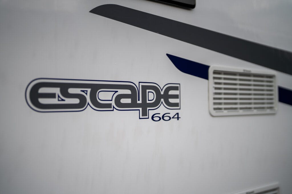 Close-up of a vehicle's side panel showing the word "Escape" in a stylized font, followed by the number "664." An air vent is visible to the right of the text. The background is a plain white surface, typical of the 2017 Swift Escape 664 model.