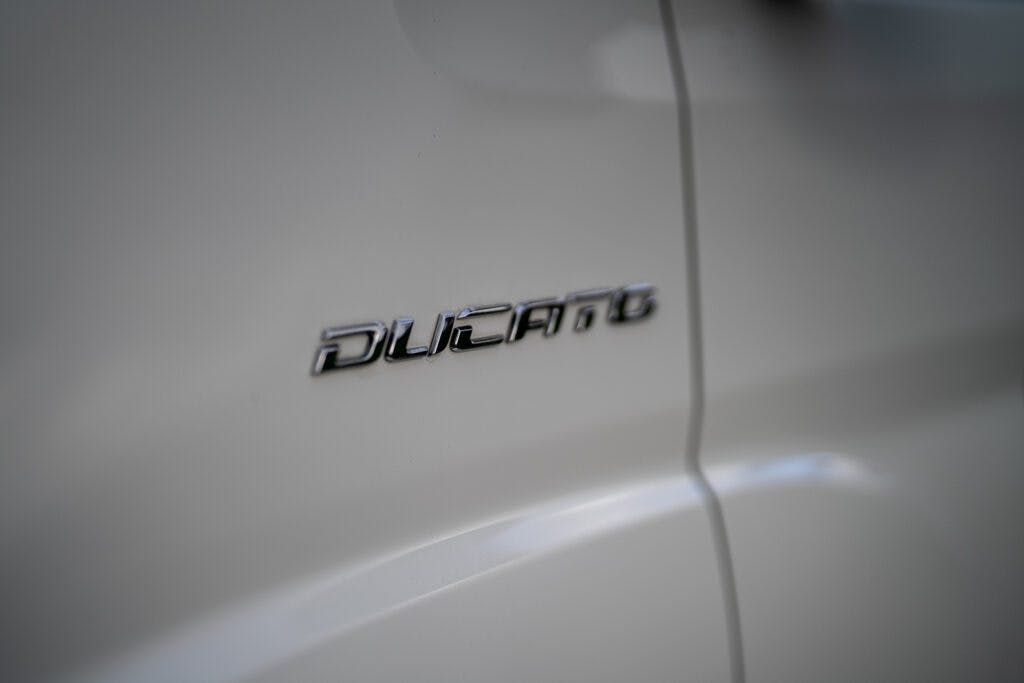 Close-up of the silver logo of a Fiat Ducato on the side of a white 2017 Swift Escape 664. The shiny metallic letters stand out against the clean background, showing a slight shadow due to the light angle.