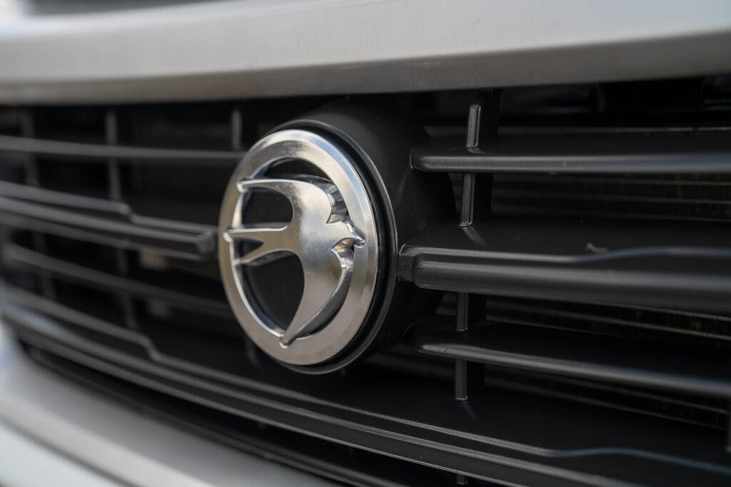Close-up of a 2017 Swift Escape 664's front grille featuring a circular emblem in the center. The emblem depicts a stylized bird in metallic silver. The grille has horizontal black slats, and part of the vehicle's front bumper is visible in the background.