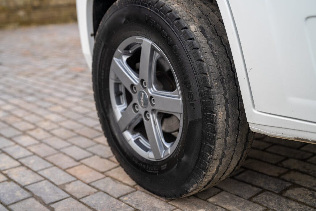 Close-up view of the rear tire and alloy wheel of a white 2017 Swift Escape 664 parked on a cobblestone pavement.