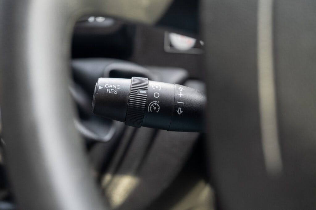 Close-up of a 2017 Swift Escape 664's steering column control lever. The lever features a rotating knob with symbols indicating wiper functions, cruise control settings, and turning indicators. The knob is surrounded by portions of the steering wheel and car interior.