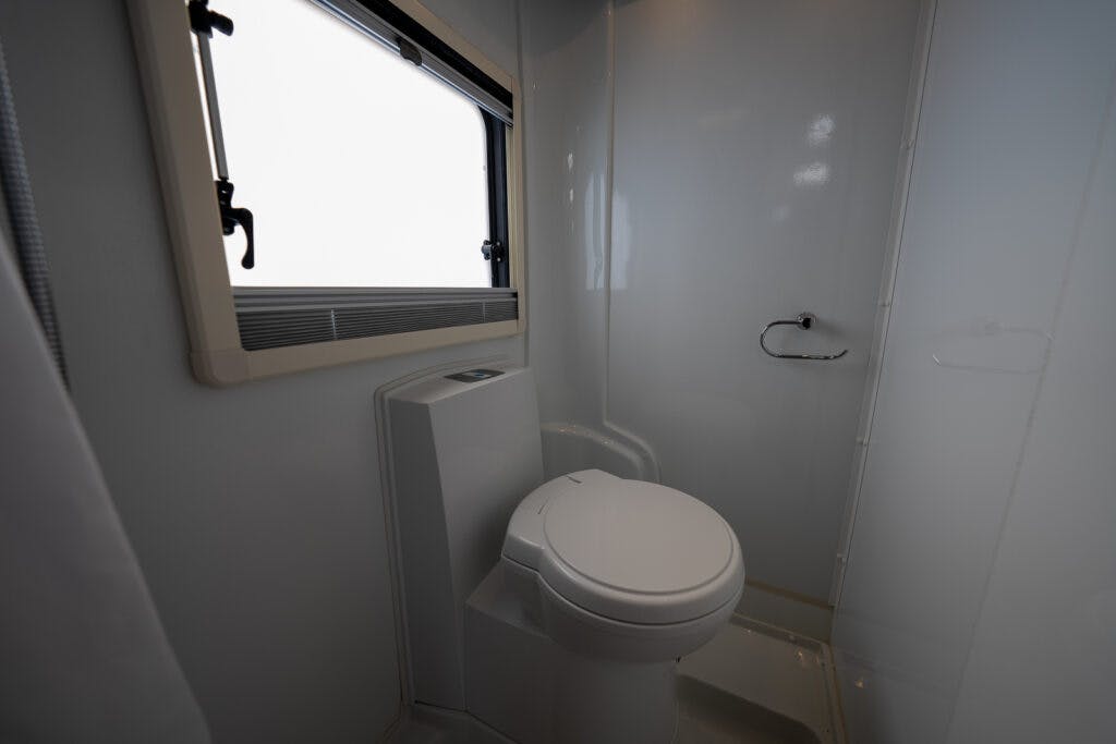 A compact bathroom in the 2017 Swift Escape 664 featuring a white toilet, a window with a handle, and a shiny wall with a towel ring. The space appears clean and modern with predominantly light-colored surfaces.