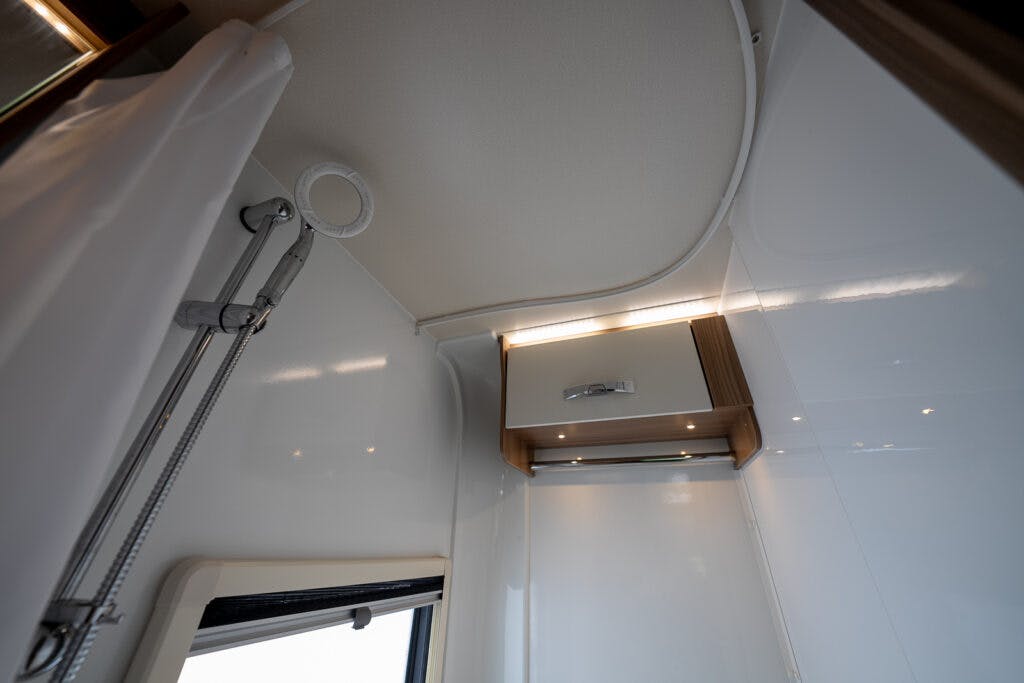 The image shows the interior of a modern bathroom, possibly from a 2017 Swift Escape 664, featuring a shower area with a mounted showerhead and a handheld shower. There is a small cabinet with a handle and under-cabinet lighting on one wall. The walls and ceiling are white and smooth.