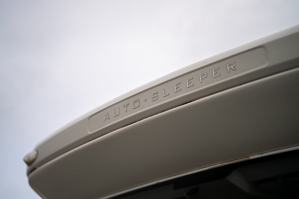 Close-up view of a portion of a 2007 Auto-Sleepers Sigma EL with the word "AUTO-SLEEPER" engraved on a panel. The image is taken from a low angle, focusing on the text against a backdrop of a cloudy sky.