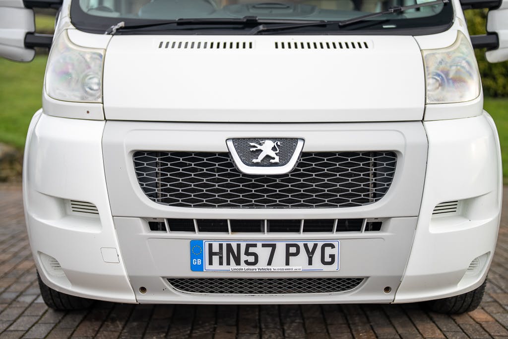 Close-up view of the front of a white Fiat van, likely a 2007 Auto-Sleepers Sigma EL, with a visible license plate reading "HN57 PYG." The grille features a Fiat logo, and the vehicle is parked on a paved area with green grass in the background.