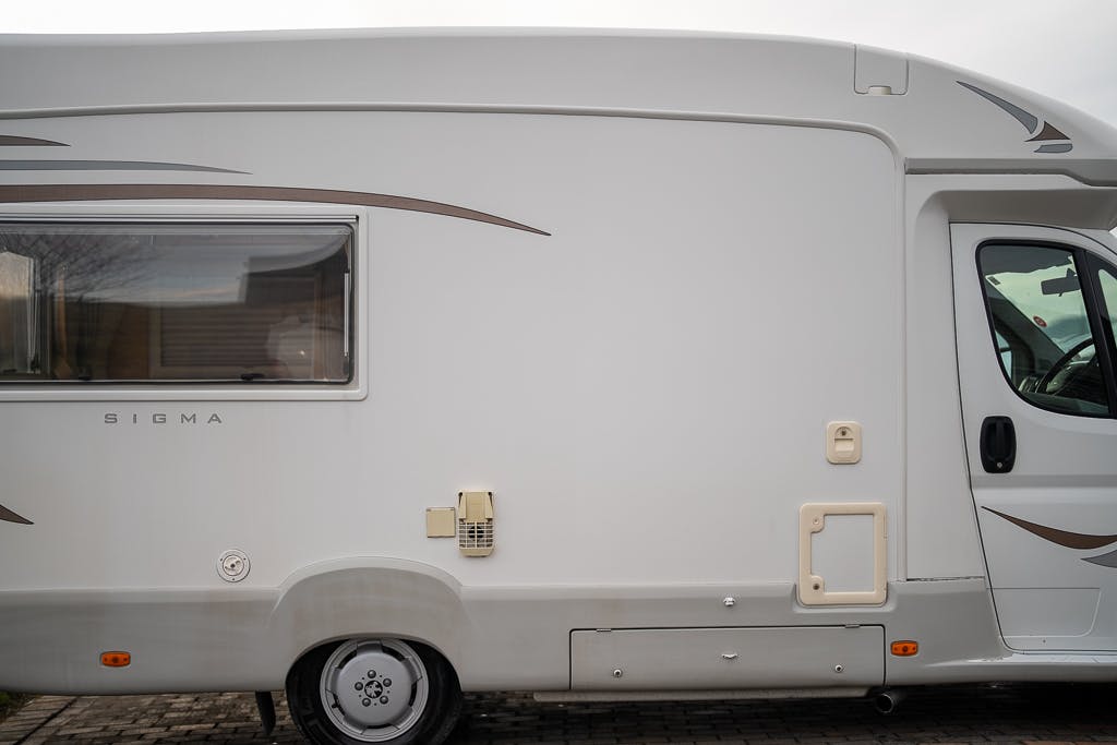 Side view of a white 2007 Auto-Sleepers Sigma EL motorhome with a single window and a door. The exterior boasts minimal brown and grey accents. The motorhome is parked on a paved surface.