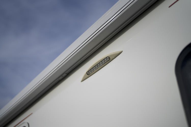 Close-up of the side of a 2014 Auto-Trail Imala 715 Lowline RV with a small light fixture. The image focuses on the top part of the RV against a backdrop of a cloudy sky.