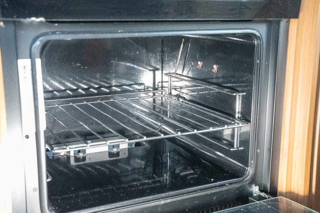 A close-up view of the interior of an empty oven with a metal rack and two temperature probes in the 2014 Auto-Trail Imala 715 Lowline. The oven's stainless steel walls are clean, and the door is open, revealing the light reflecting inside.