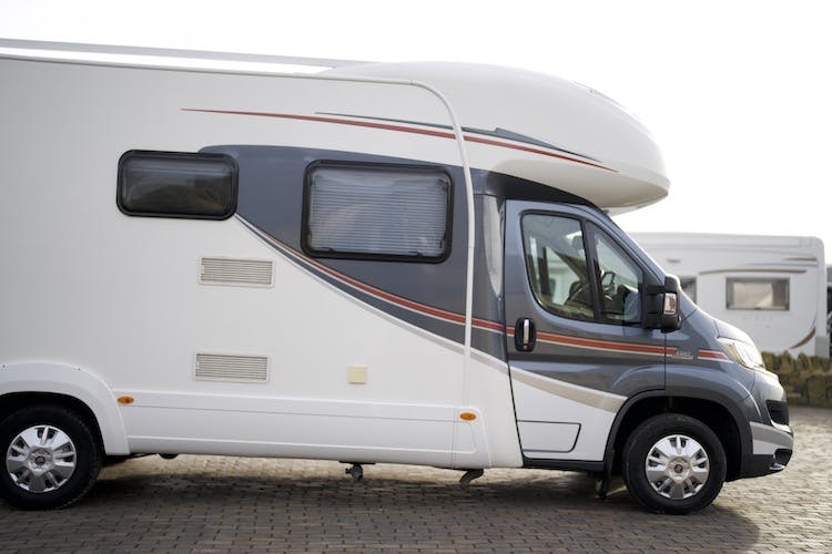A white and gray 2014 Auto-Trail Imala 715 Lowline motorhome is parked on a cobblestone surface. The vehicle features a streamlined design with a large side window and a door on the right side. Another similar motorhome is partially visible in the background.