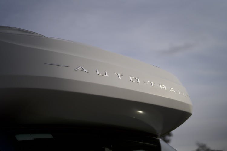 Close-up of the top part of a vehicle, showing the word "Auto-Trail" on it. The image appears to have been taken at dusk or dawn, with the sky in the background partly cloudy. This 2014 Auto-Trail Imala 715 Lowline model captures a serene moment against a picturesque sky.