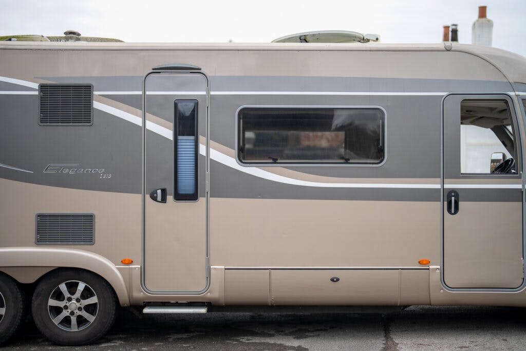 A beige and gray 2013 Burstner Elegance 810 G RV is parked on a paved surface. It has a side entry door with a small window, a larger rectangular window, and several vent panels. The RV features three visible wheels and roof-mounted vents.