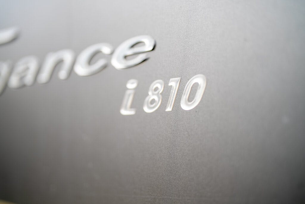 Close-up of text on a smooth, metallic surface showing the characters "i 810." The text is embossed, with "i 810" prominently displayed in focus, reminiscent of the fine detailing found on the 2013 Burstner Elegance 810 G. The rest of the text is partially visible and slightly blurred.