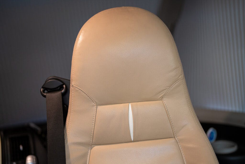 The image shows the backrest of a beige leather seat in a 2013 Burstner Elegance 810 G, with a single, subtle horizontal crease in the center. A black seatbelt is visible on the left side. The background appears to be part of a vehicle interior.
