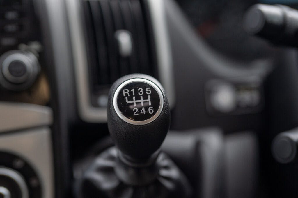 Close-up image of a car's manual gear shift knob in the 2019 Elddis Autoquest 196 Signature Edition. The knob displays the gear shift pattern with six forward gears and one reverse, labeled "R 1 3 5" on the top row and "2 4 6" on the bottom row. The background shows part of the car's dashboard.