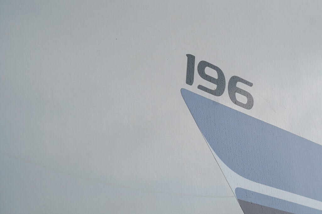 The image depicts a close-up view of the exterior of an aircraft. The number "196" is prominently displayed on the side, accompanied by a blue and gray stripe reminiscent of the 2019 Elddis Autoquest 196 Signature Edition. The background is a plain, light color, likely the body of the aircraft.