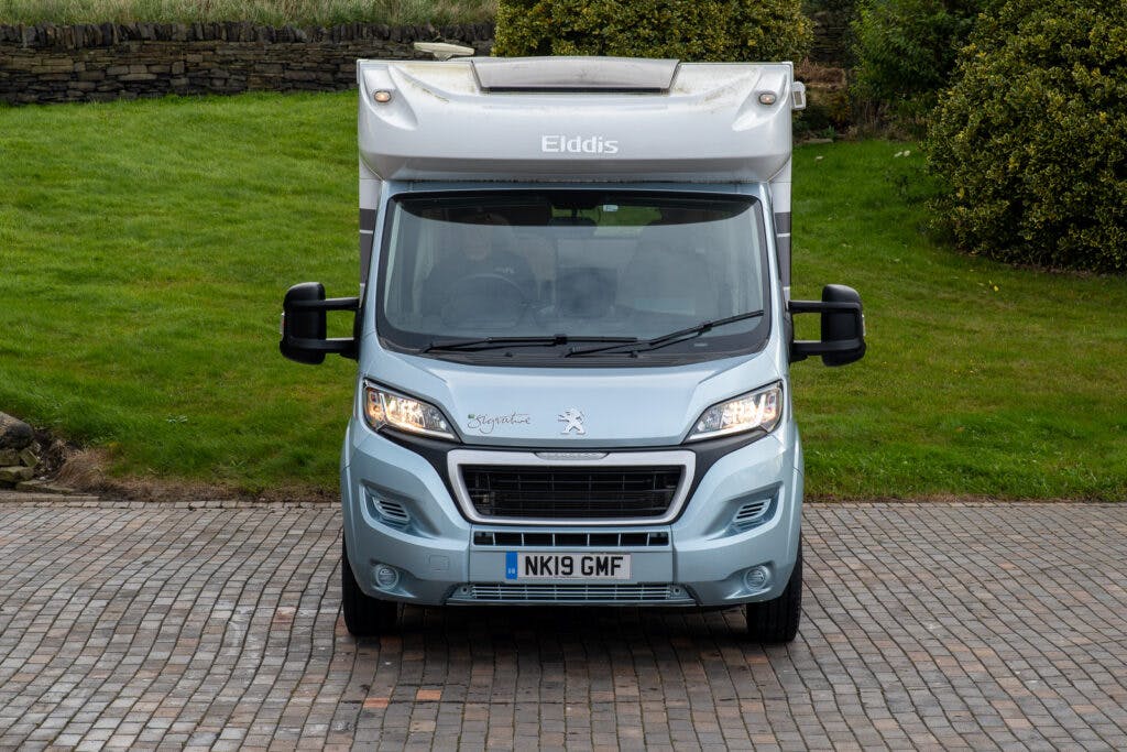 A silver 2019 Elddis Autoquest 196 Signature Edition motorhome parked on a cobblestone driveway with a grassy area and stone wall in the background. The front license plate reads "NK19 GMF.