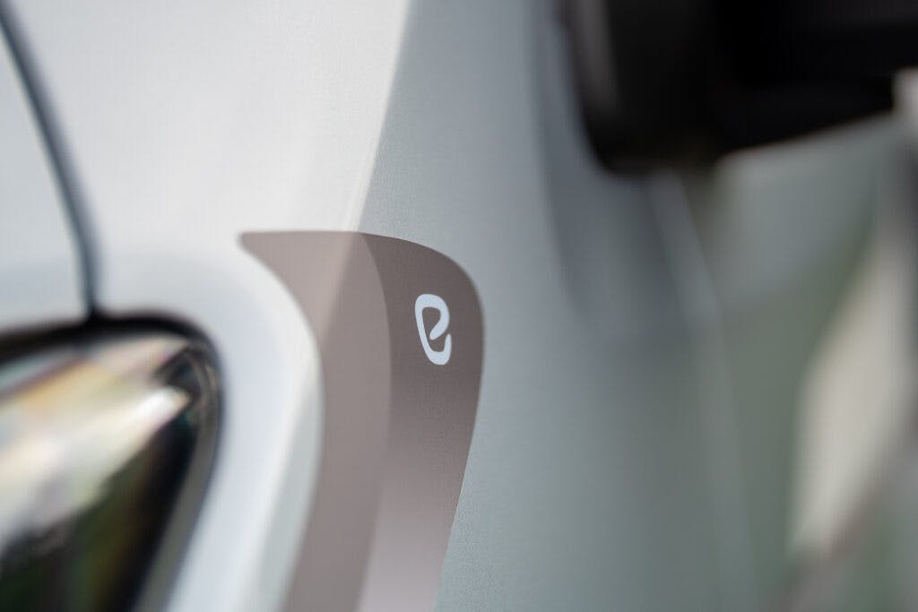 Close-up photo of a light grey vehicle showing the sleek design detail near the front. The image focuses on a small, white logo with a stylized "e" on the grey panel, next to a black component of the 2019 Elddis Autoquest 196 Signature Edition. The background is slightly blurred.