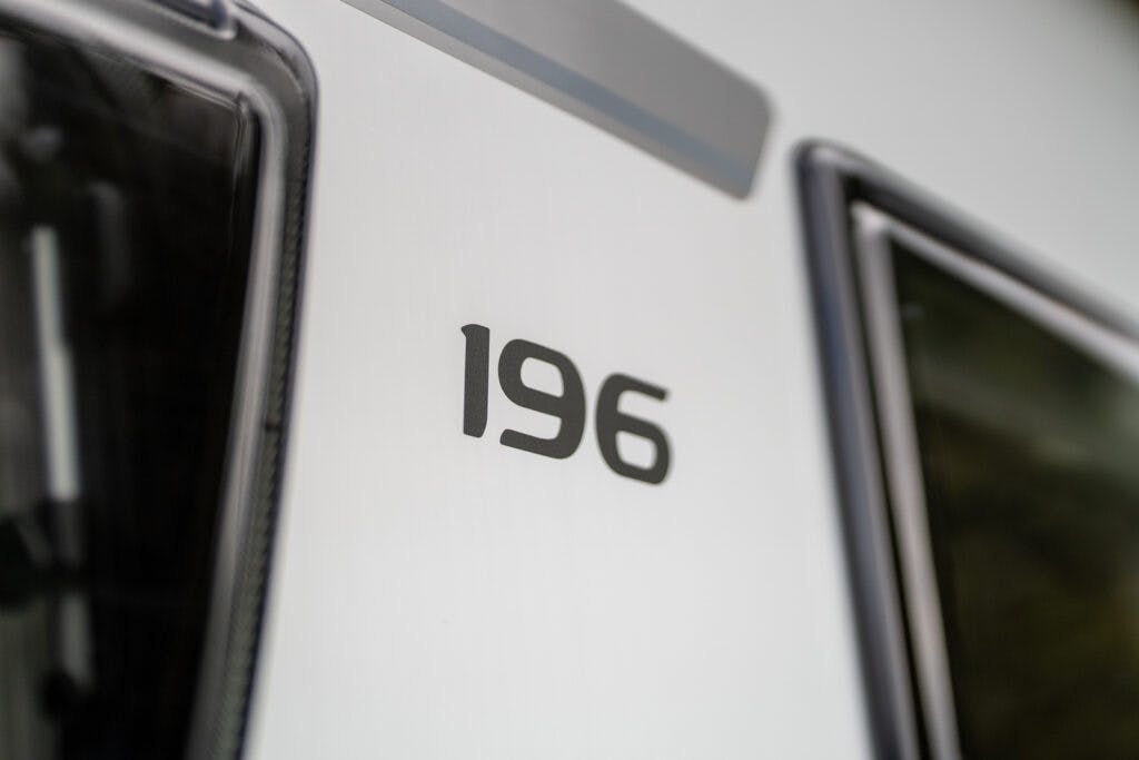 The image shows the number 196 printed on the side of a white vehicle, specifically a 2019 Elddis Autoquest 196 Signature Edition, with partial views of two windows on either side. The photo has a close-up perspective, focusing on the number.
