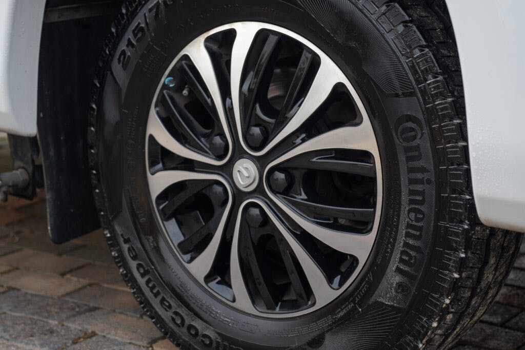 Close-up view of a Continental tire and black alloy wheel on a 2019 Elddis Autoquest 196 Signature Edition. The wheel features an intricate design with multiple spokes. The tire has visible tread patterns and text indicating it's a Continental brand tire. The background shows a brick pavement.