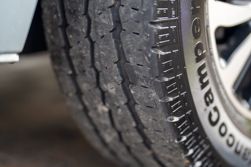 Close-up image of a worn-out tire on a vehicle, showing visible wear on the tread pattern. The sidewall indicates the tire brand and model. The camera focuses on the lower part of the tire, emphasizing the need for replacement, particularly if it's from a 2019 Elddis Autoquest 196 Signature Edition.