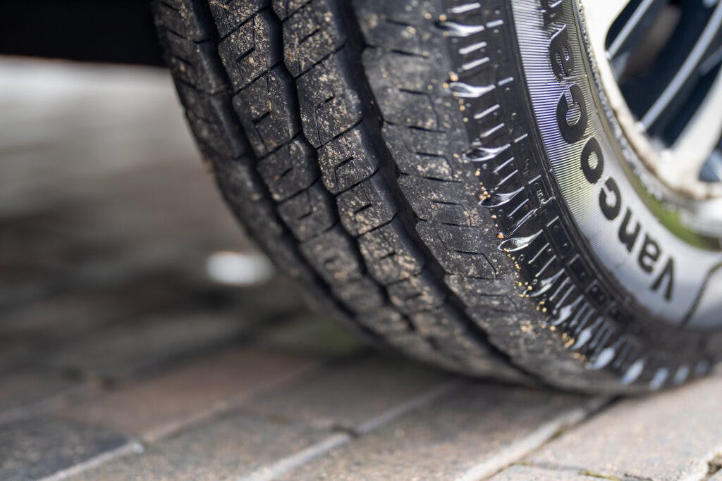 Close-up of a vehicle tire showing its detailed tread pattern. The tire, part of the 2019 Elddis Autoquest 196 Signature Edition, is partially on a paved surface with some dust and small debris on its surface. The brand name "Vanco" is visible on the sidewall. The image focuses on the lower part of the tire.