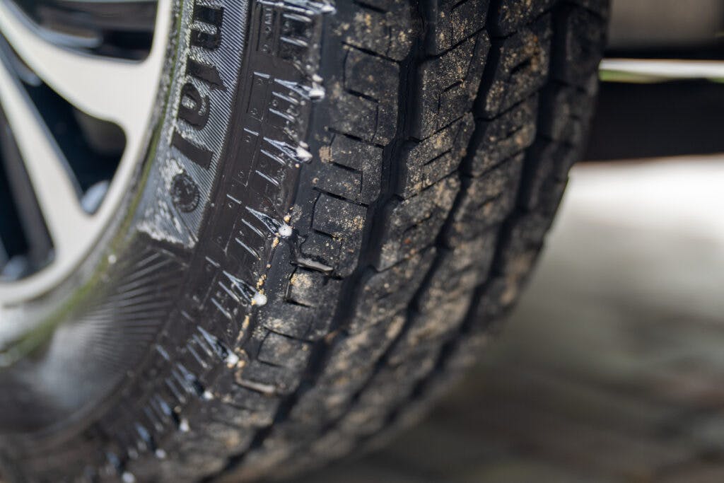 Close-up of a car tire on the 2019 Elddis Autoquest 196 Signature Edition, showing intricate tread patterns and slight traces of dirt. The tire is mounted on a wheel, the edge of which is partially visible on the left side of the image. The background is blurred.