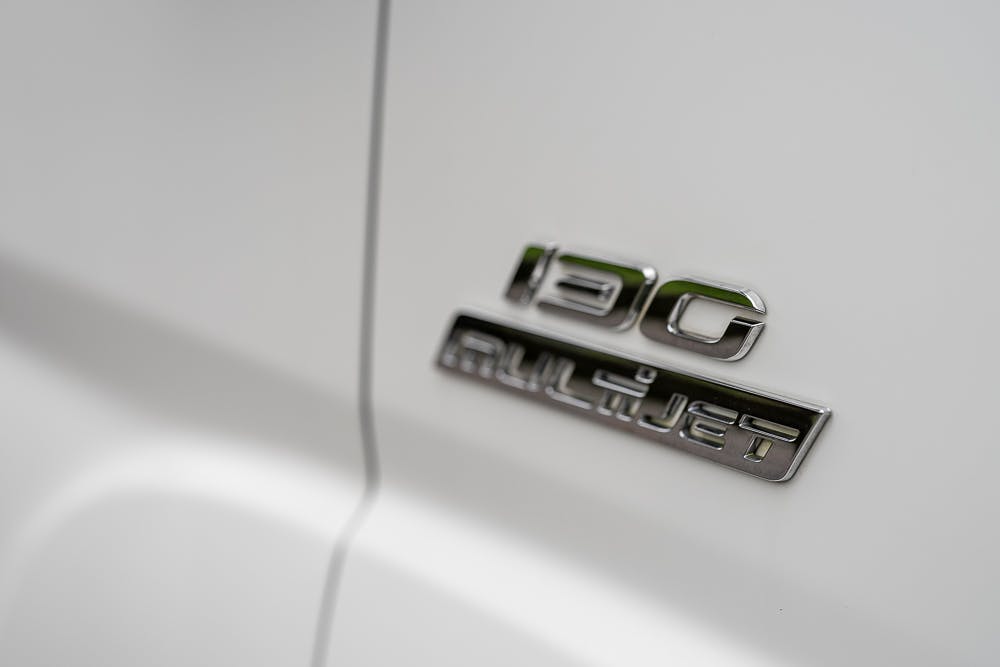 Close-up of a 2016 Roller Team Auto-Roller 707 Low Line with a chrome badge displaying the text "190 MULTIJET" on a white surface. The image focuses on the badge, capturing the polished look of the lettering.