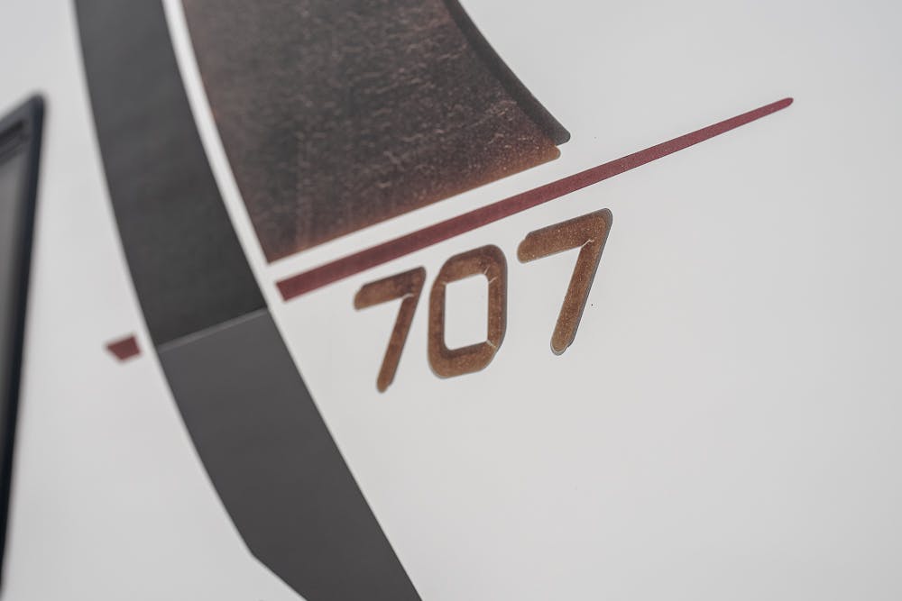 Close-up of a design on a white surface, featuring the number "707" in brown, with a red line intersecting it diagonally. Adjacent to the number is part of a black and brown pattern, reminiscent of the sleek aesthetics found on the 2016 Roller Team Auto-Roller 707 Low Line.
