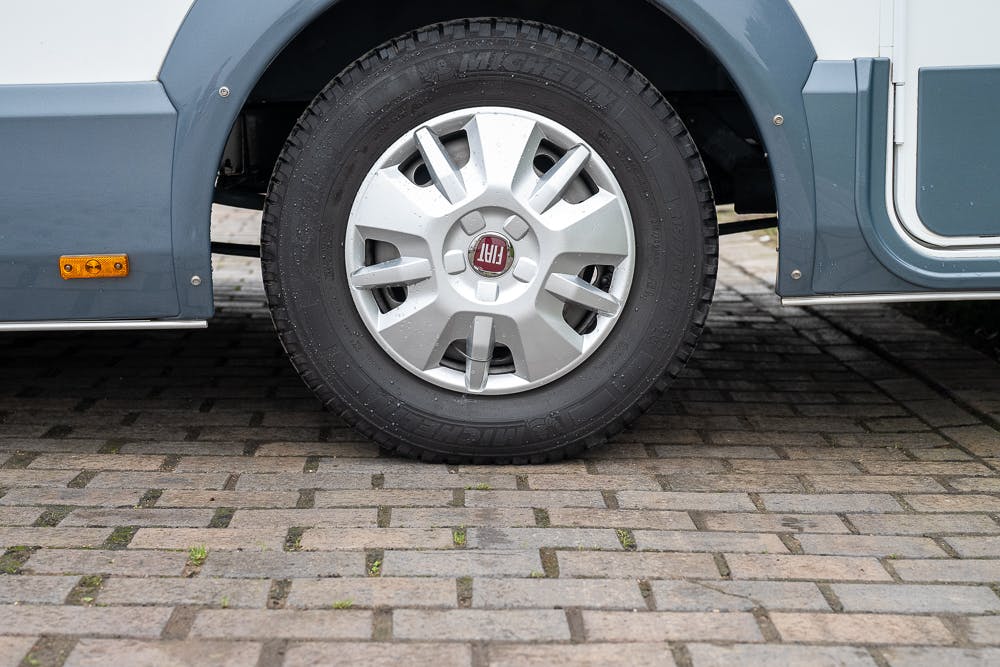 Close-up image of a Fiat car wheel with a Michelin tire, parked on a brick pavement. The vehicle, which appears to be part of a 2016 Roller Team Auto-Roller 707 Low Line, has bodywork partially visible in white and gray. The wheel features a silver alloy rim with the Fiat logo in the center.