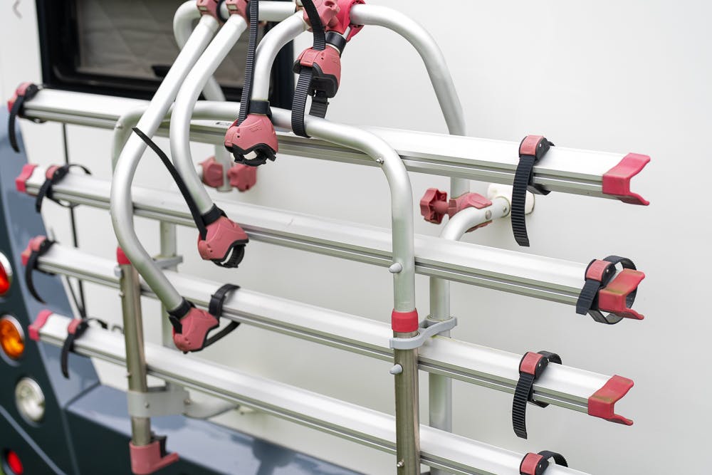 A close-up view of a mounted bike rack attached to the back of a 2016 Roller Team Auto-Roller 707 Low Line. The rack has multiple slots for holding bicycles securely, with several straps and clamps for fastening. The rack and part of the vehicle's rear are in clear focus.