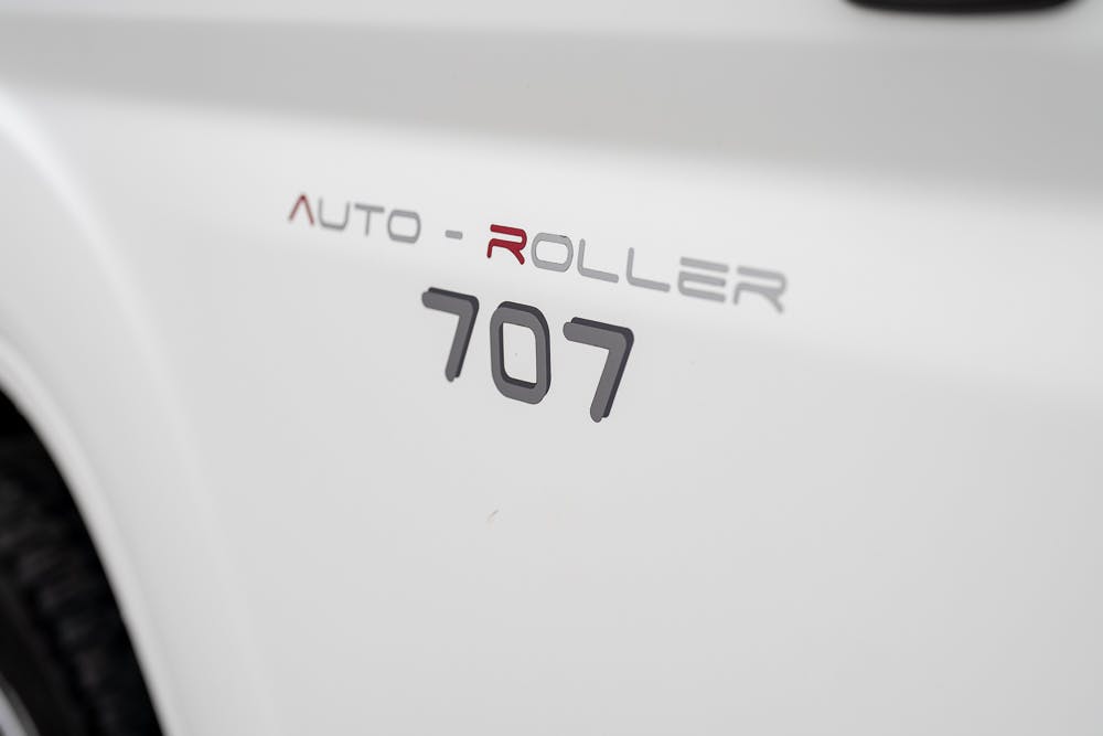 Close-up image of a white vehicle's side panel with "2016 Roller Team Auto-Roller 707 Low Line" written on it. The text is in a metallic and red font. The vehicle's tire is partially visible on the left side.