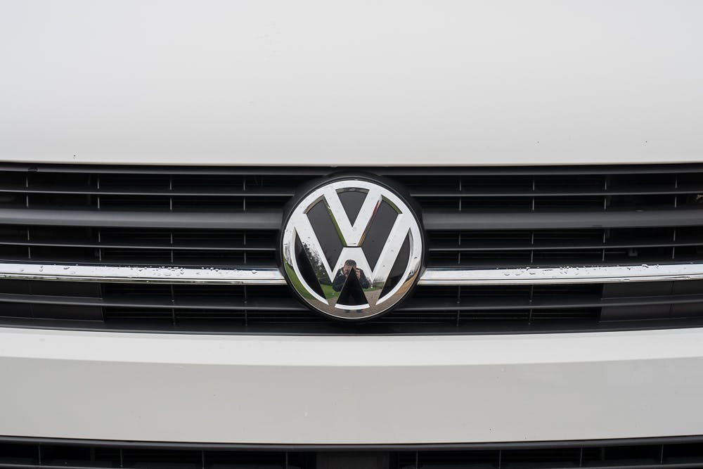 Close-up shot of the Volkswagen logo on the front grill of a white 2019 Volkswagen Transporter T28 Trendline TDI. The VW emblem is centered on a black grill with horizontal slats.