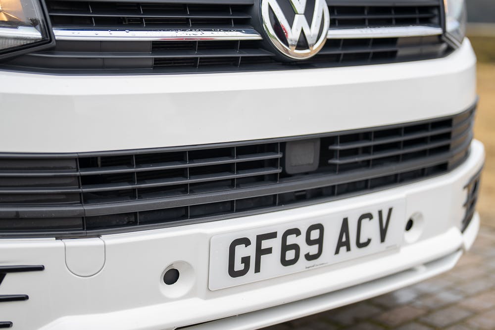 Close-up view of the front grille and license plate of a white 2019 Volkswagen Transporter T28 Trendline TDI. The license plate reads GF69 ACV, and the Volkswagen logo is prominently displayed above the grille.