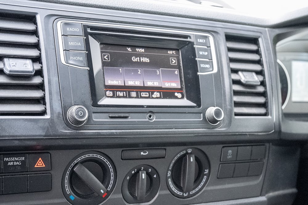 The dashboard of the 2019 Volkswagen Transporter T28 Trendline TDI features a radio screen with "Grt Hits" selected, accompanied by buttons for radio stations, media, phone, and setup. Rotary dials and buttons for climate control are situated below along with a passenger airbag indicator.