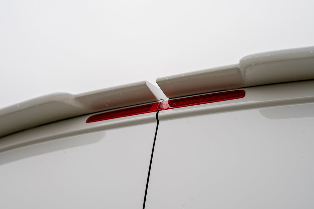 Close-up image of the rear upper portion of a white 2019 Volkswagen Transporter T28 Trendline TDI, focusing on the red brake light and a seam where two parts of the vehicle meet. The surface shows slight indications of wetness likely due to rain. The background is overcast.