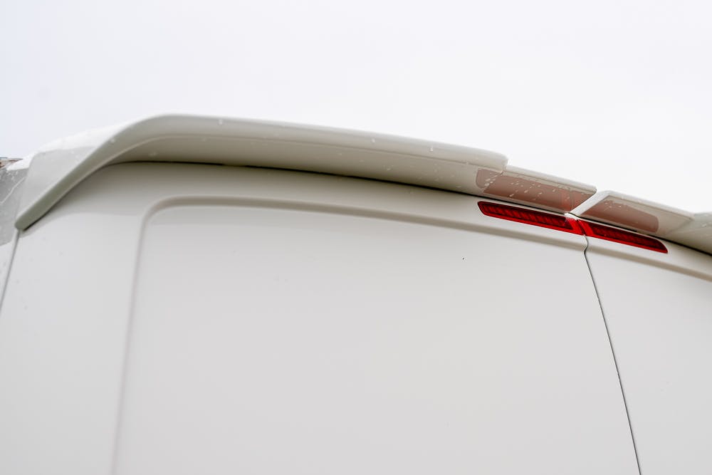 Close-up of the rear section of a 2019 Volkswagen Transporter T28 Trendline TDI, highlighting the upper edge of the back door and the integrated brake light on a cloudy day. The image shows minimal detail of the van’s surface and door seams.