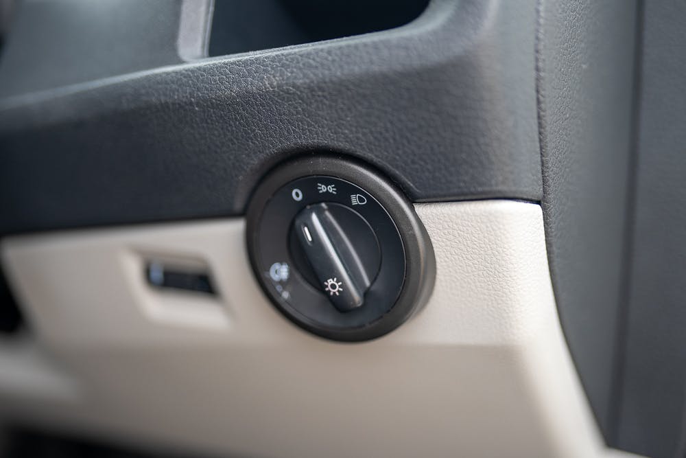 Close-up of a car headlight control switch on the dashboard panel of a 2019 Volkswagen Transporter T28 Trendline TDI. The switch has four positions: off, headlights, parking lights, and automatic setting. The dashboard panel features a combination of black and beige colors.