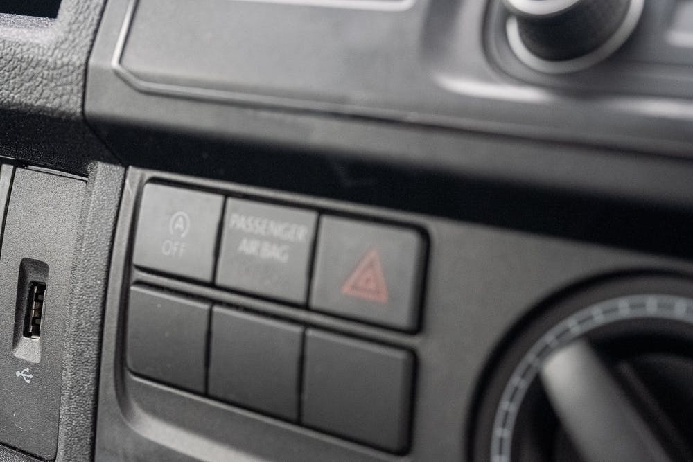 Close-up of a 2019 Volkswagen Transporter T28 Trendline TDI dashboard showing controls for a passenger airbag and hazard lights. The passenger airbag button is clearly marked "PASSENGER AIRBAG" with "ON" and "OFF" options, and a red triangle symbol represents the hazard lights button.