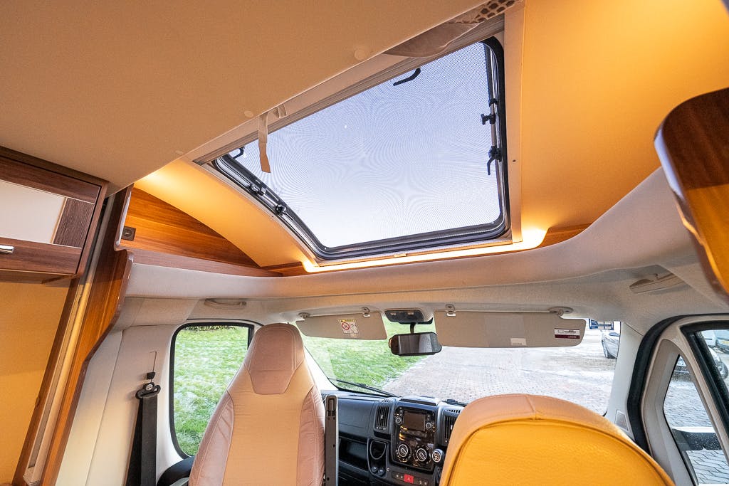 Interior view of a 2016 Roller Team Auto-Roller 707 Low Line camper van looking towards the front seats. The roof has a large skylight with lighting around it. The dashboard is equipped with controls and a rearview mirror. The driver's seat is on the left, and the passenger seat is on the right.