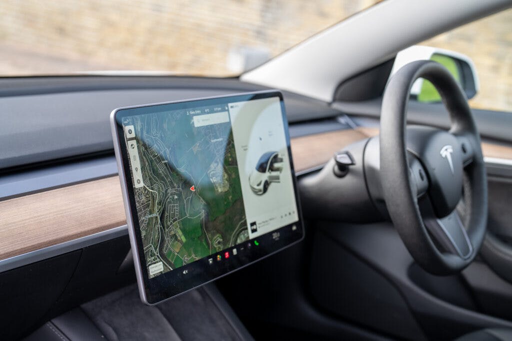 The interior of the 2021 Tesla Model 3 Long Range AWD showcases the dashboard and steering wheel, with a large touchscreen display in the center. The screen displays a navigation map and vehicle information. Visible are sleek design elements and ambient lighting.