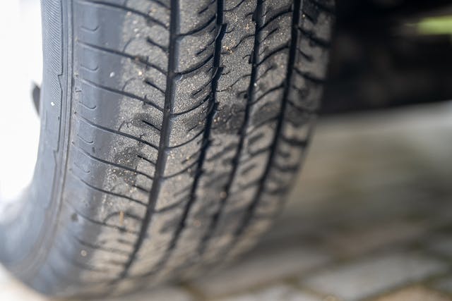 Close-up view of a car tire with visible dirt and wear on the treads, indicating use. The tire is mounted on a 2019 Benimar Tessoro T486. The background is blurred, focusing attention on the tire's surface and tread pattern.