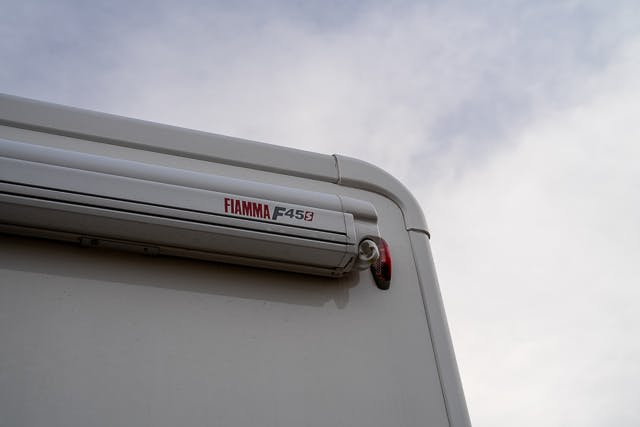 Close-up view of the back corner of a 2019 Benimar Tessoro T486 with a Fiamma F45s awning mounted on it. The sky in the background is cloudy.