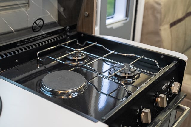 The image shows a close-up of a two-burner gas stove with shiny metal grates inside the 2019 Benimar Tessoro T486. Two knobs are visible on the right side of the stove, with two additional knobs partially out of frame. The stove is installed in what appears to be a compact kitchen area.