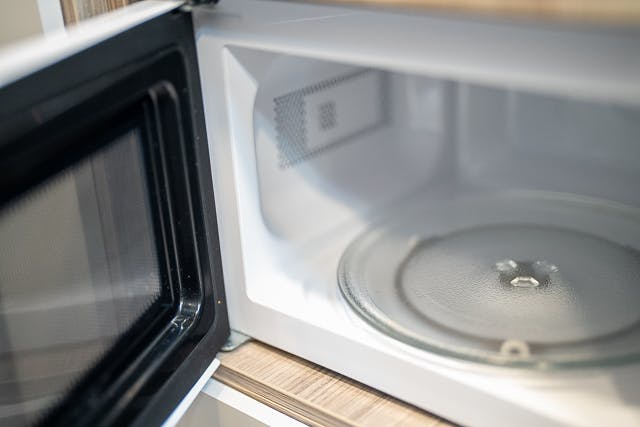 A 2019 Benimar Tessoro T486 microwave with its door open, revealing a clean and empty interior. The glass turntable is in place at the bottom, and the inside is predominantly white with light wood trim around the opening.