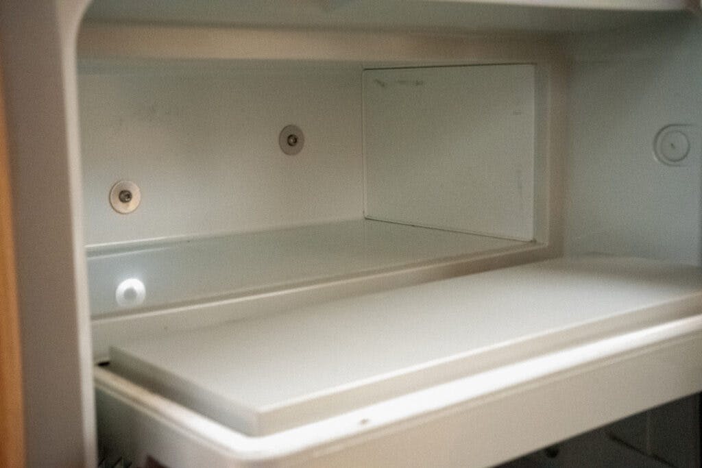 The image shows the interior of an empty refrigerator shelf inside a 2006 Auto-Sleepers Nuevo EK, with a white, smooth surface and a back panel. The shelf is clean and devoid of any contents or items.