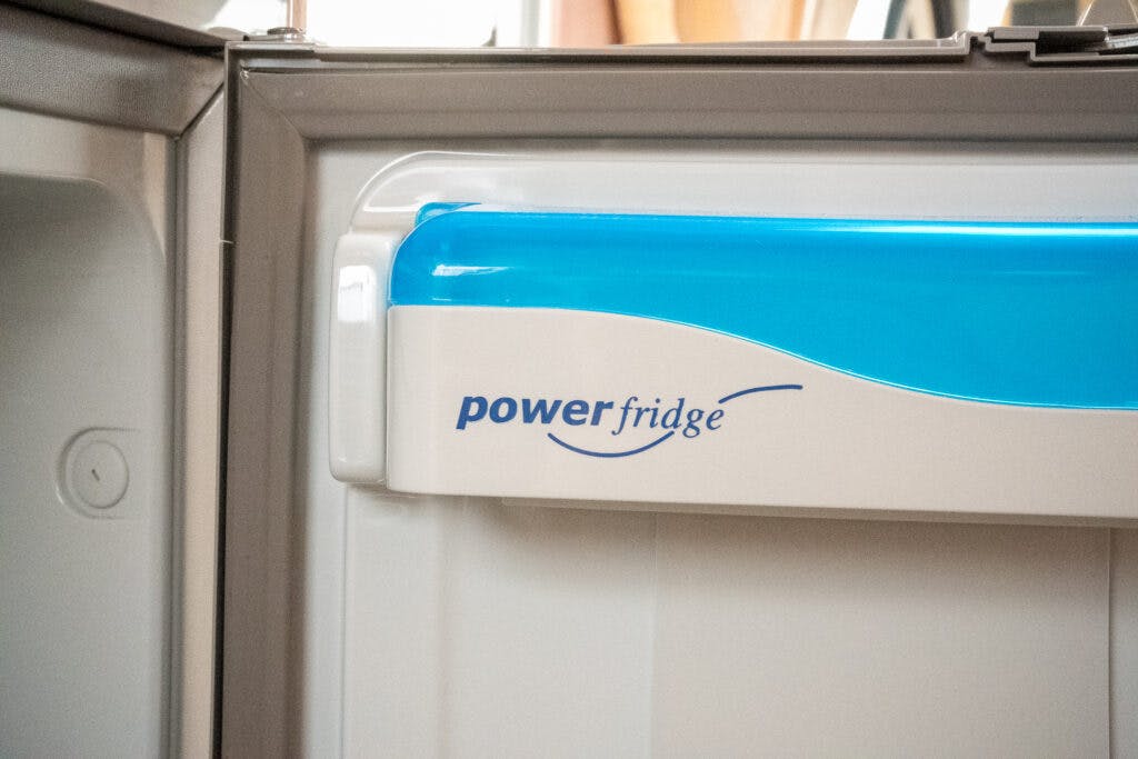 A close-up view of the interior of a fridge door in a 2006 Auto-Sleepers Nuevo EK, featuring a blue and white compartment labeled "powerfridge." The compartment is part of a larger refrigerator unit, with the door partially open, exposing the sealing edge and some interior space.
